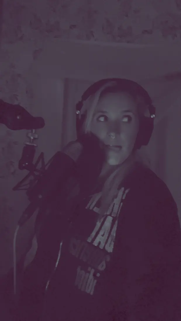 Nikyla in headphones at the microphone, glancing sideways in a dim room.